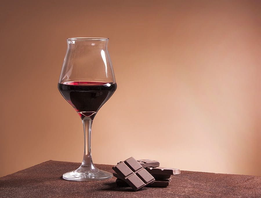 Glass of wine sitting next to a pile of chocolates.