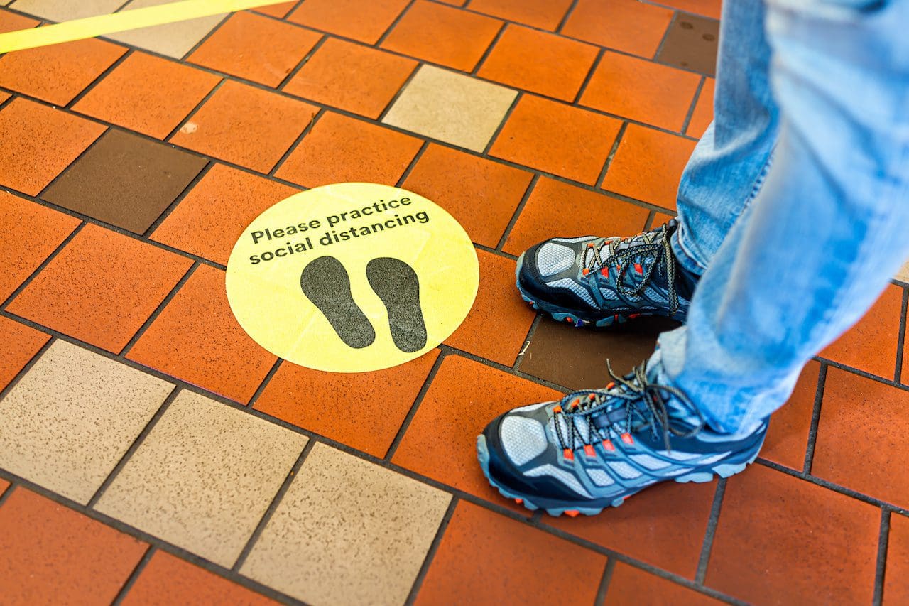 Yellow warning sign to maintain social distance distancing during covid-19 coronavirus outbreak with footsteps in store and legs of person in USA