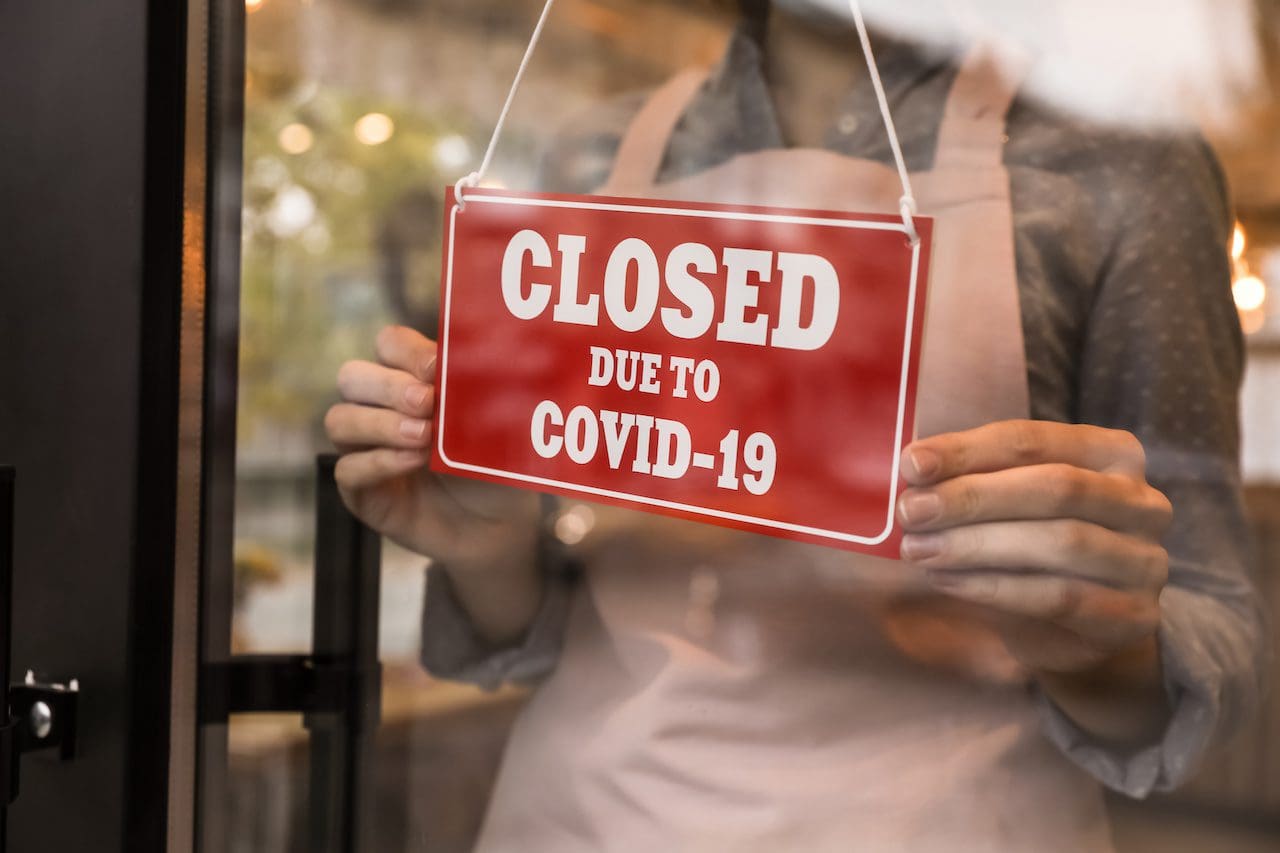 Woman putting red sign with words “Closed Due To Covid-19” onto glass door, closeup