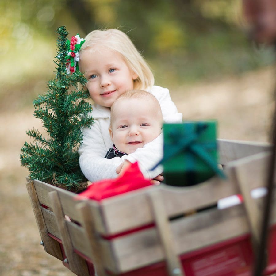 Baby Brother and Sister Being Pulled in Wagon with Christmas Tree and Gifts Outdoors.